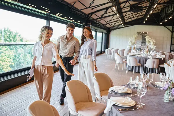 Bankettkoordinator zeigt glücklichen verliebten Paaren festliche Tische im Veranstaltungssaal mit Hochzeitsdekor — Stockfoto