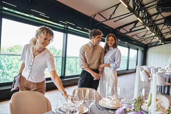 Glückliches verliebtes Paar in der Nähe von Eventmanager und Tischen mit festlichem Rahmen im modernen Bankettsaal — Stockfoto