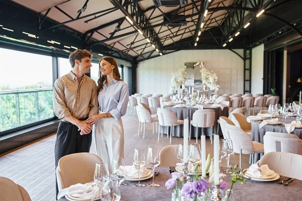 Glückliches verliebtes Paar, das sich in der Nähe des festlichen Tisches in der Veranstaltungshalle anschaut, Brautvorbereitung — Stockfoto