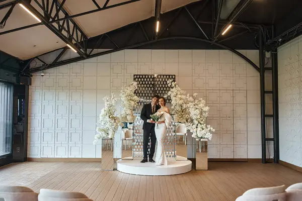 Larga duración de los recién casados felices en salón de banquetes decorado con flores blancas en flor, día especial - foto de stock