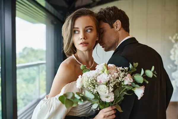 Charming bride with wedding bouquet looking away near groom in  black suit in banquet hall — Stock Photo