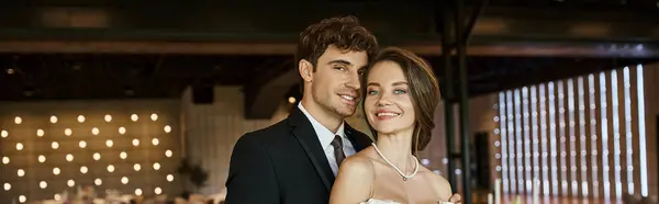 Jeune et joyeux couple de jeunes mariés en souriant à la caméra dans la salle de célébration décorée, bannière — Photo de stock