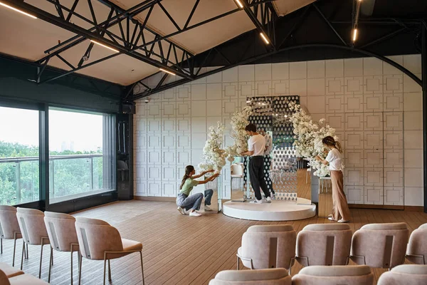 Команда декораторів, що влаштовують білі квіткові композиції в сучасному бенкетному залі, творчі роботи — стокове фото