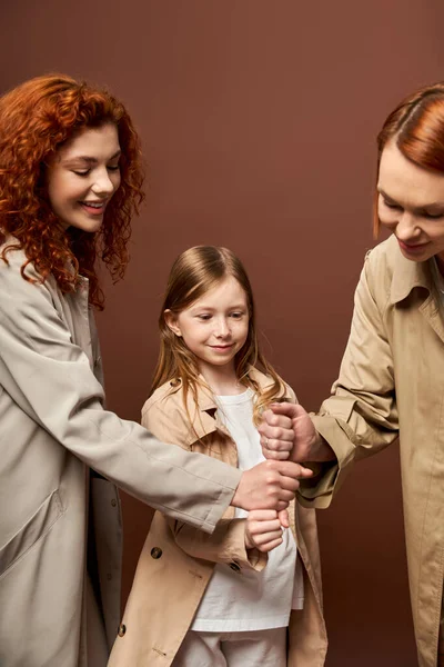Generations, happy family with red hair stacking hands together on brown backdrop, women and girl — Stock Photo