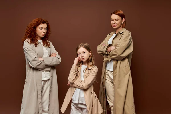 Tre generazioni, donne in posa cappotti e guardando il bambino su sfondo marrone, famiglia rossa — Foto stock