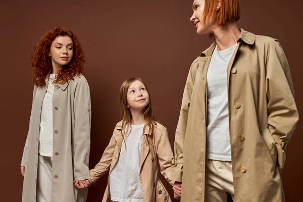 Três gerações, mulheres de casacos de mãos dadas com a menina feliz no fundo marrom, família ruiva — Fotografia de Stock