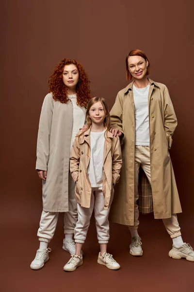 Geração feminina, família ruiva em pé juntos em outerwear no fundo marrom, mulheres e menina — Fotografia de Stock