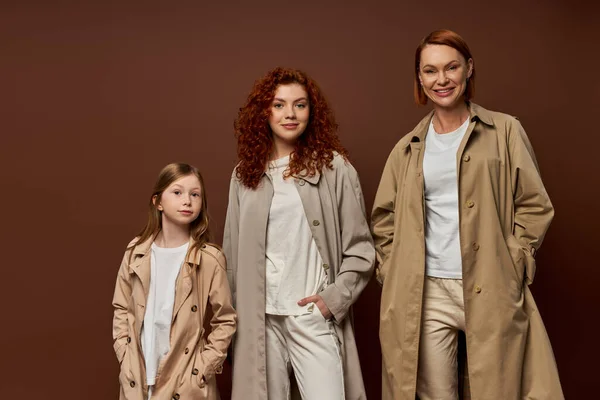 Generazione femminile 'famiglia con capelli rossi in posa con le mani in tasche in capispalla su sfondo marrone — Foto stock