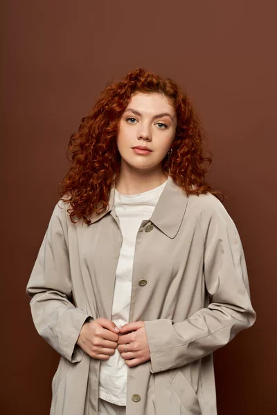 Beautiful woman with red curly hair posing in autumn coat on brown background, fall season — Stock Photo