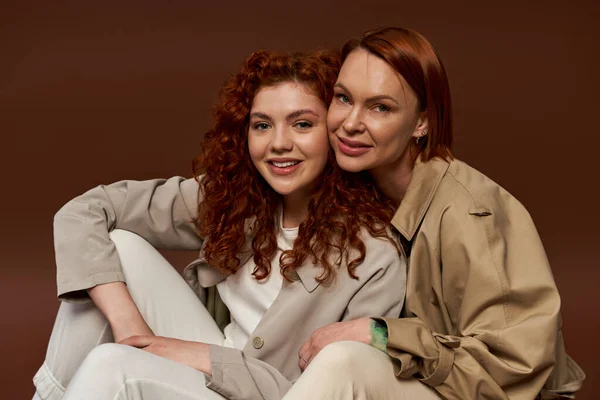 Deux générations, femmes gaies aux cheveux roux posant en tenue d'automne à la mode sur fond brun — Photo de stock