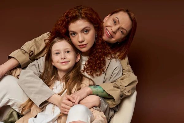 Три поколения, позитивная рыжая семья, смотрящая на камеру на коричневом фоне, современная пародия — стоковое фото