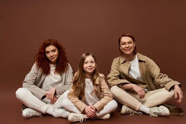 Happy redhead family of three female generations sitting and looking at camera, autumn coats — Stock Photo