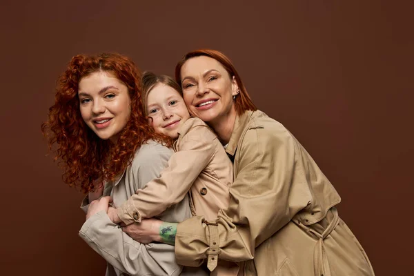 Happy redhead family of three female generations hugging on brown background, autumn fashion — Stock Photo