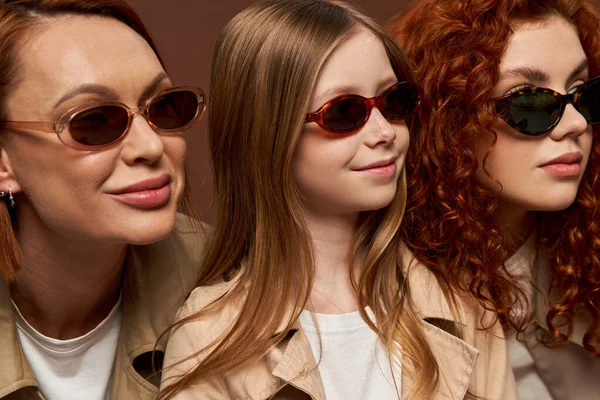 Family generation change concept, portrait of redhead women and girl in sunglasses on brown backdrop — Stock Photo
