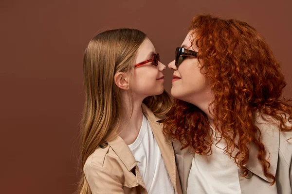 Two generations, happy redhead mother and daughter in sunglasses on brown backdrop, face to face — Stock Photo