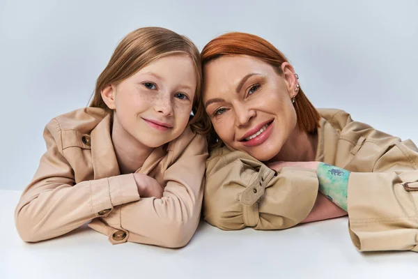 Felice due generazioni, donna rossa e bambino in trench beige sorridenti su sfondo grigio — Foto stock