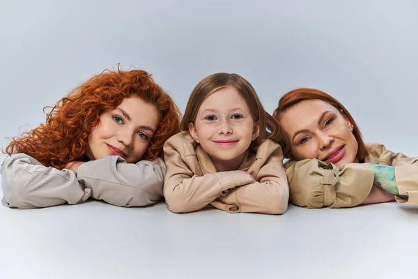 Felici generazioni femminili, donne rosse e bambini in cappotti beige sorridenti su sfondo grigio, famiglia — Foto stock