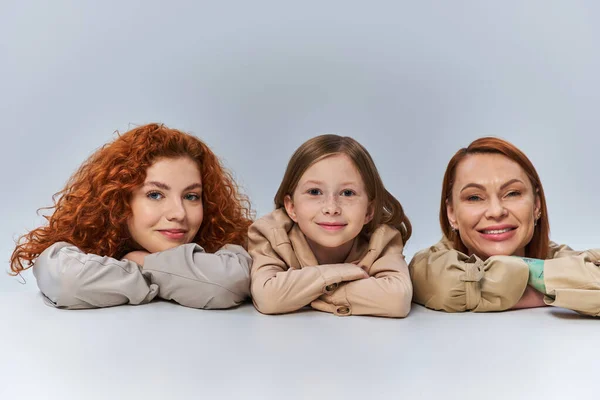 Gioiose generazioni femminili, donne rosse e bambini in cappotti beige sorridenti su sfondo grigio, famiglia — Foto stock