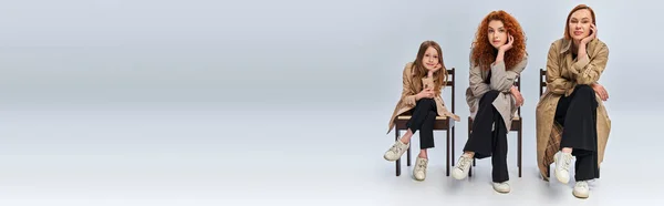 Weibliche Generationen, glückliche rothaarige Frauen und Kinder, die in Reihen auf Stühlen vor grauem Hintergrund sitzen — Stockfoto