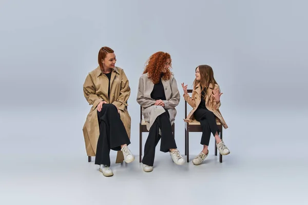 Três gerações, menina ruiva conversando com seus parentes e sentado em cadeiras em pano de fundo cinza — Fotografia de Stock