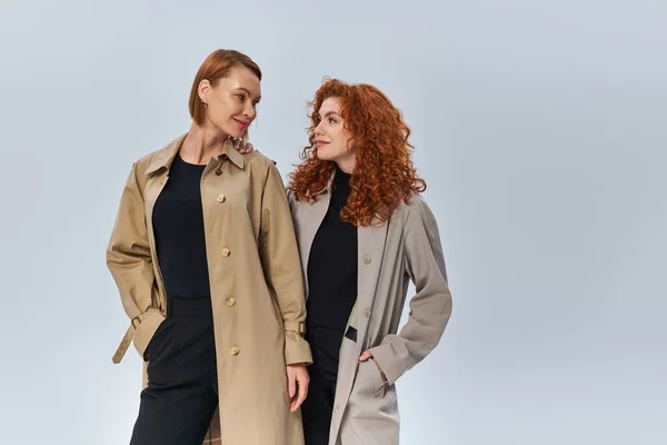 Deux générations de femmes rousses posant en manteau et se regardant sur fond gris — Photo de stock