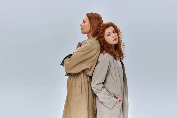 Duas gerações de mulheres ruivas de pé em casacos de trincheira em fundo cinza, moda outono — Fotografia de Stock