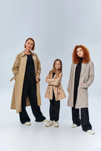 Famiglia rossa in posa cappotti con le mani in tasca su sfondo grigio, felici generazioni femminili — Foto stock