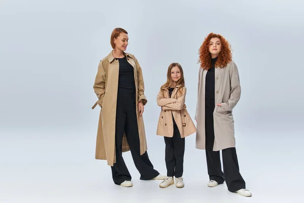Руда сім'я в пальто позує і стоїть разом на сірому фоні, щасливі жіночі покоління — стокове фото