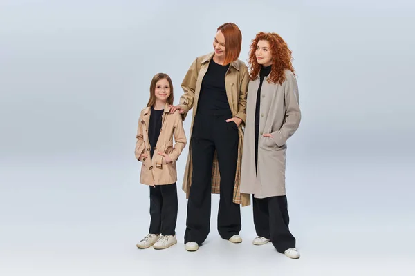 Руда сім'я в осінніх пальто позує руками в кишенях на сірому тлі, три покоління — стокове фото