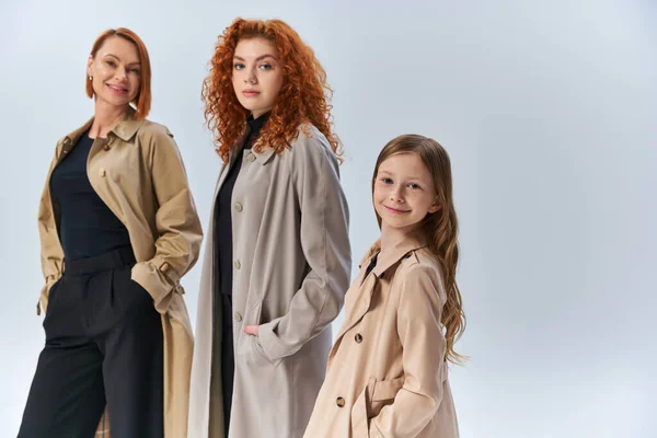 Happy redhead family in stylish coats posing with hands in pockets on grey , three generations — Stock Photo