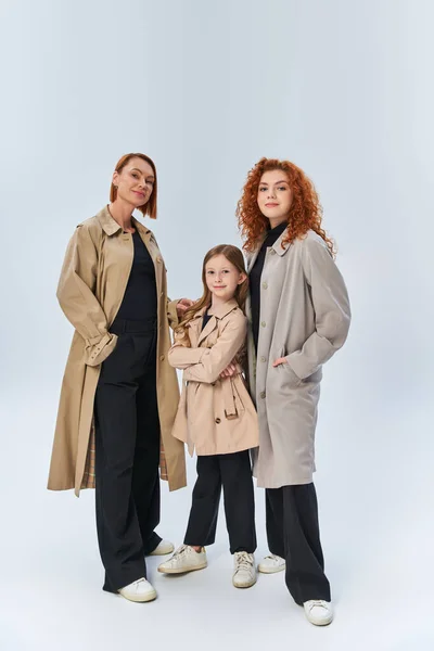 Tre generazioni allegra famiglia in piedi insieme in eleganti cappotti su sfondo grigio, moda autunno — Foto stock