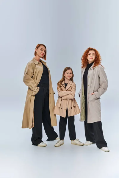 Три покоління рудоволоса сім'я позує разом в осінніх пальто на сірому фоні, повна довжина — стокове фото