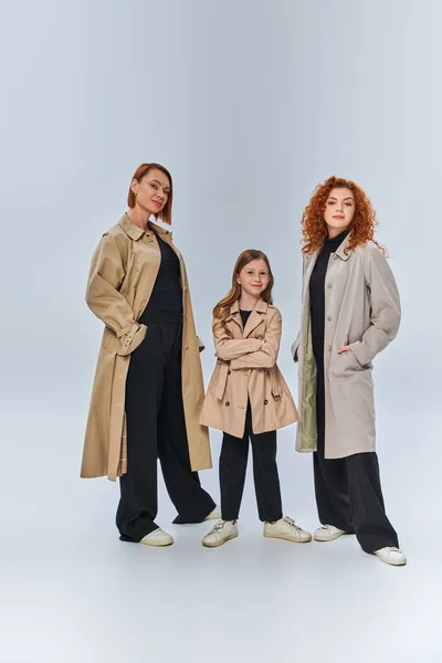 Famille de rousses de trois générations posant ensemble en manteaux d'automne sur fond gris, pleine longueur — Photo de stock