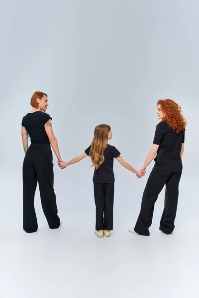 Female generations, happy redhead family holding hands and standing in matching attire on grey — Stock Photo