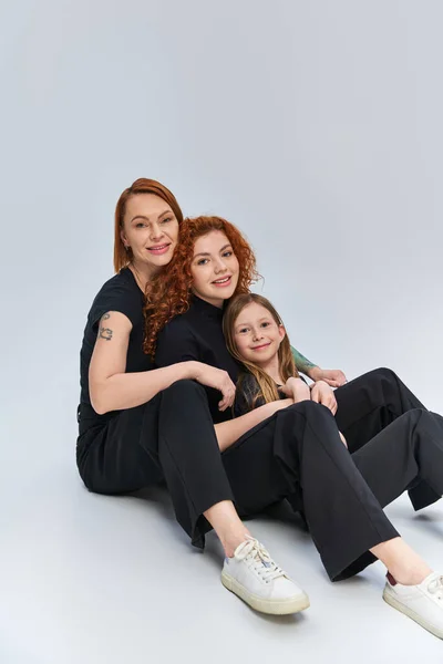 Rothaarige Familie in passenden Outfits, die sich umarmen und vor grauem Hintergrund zusammensitzen, drei Generationen — Stockfoto