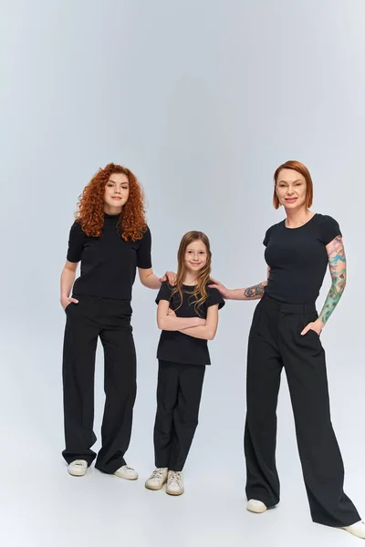 Famiglia rossa in abiti coordinati in piedi insieme su sfondo grigio, tre generazioni femminili — Foto stock