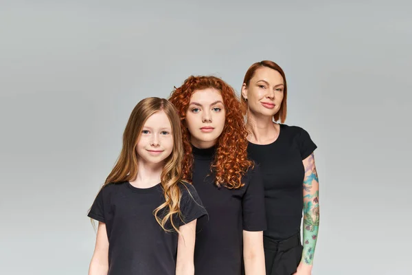 Portrait of women red hair posing with girl in matching outfits on grey backdrop, three generations — Stock Photo