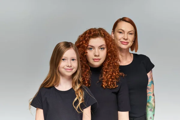 Joyful women red hair posing with girl in matching outfits on grey backdrop, three generations — Stock Photo