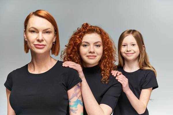 Drei Generationen fröhlicher Frauen und Mädchen posieren in passenden Outfits vor grauem Hintergrund, Familie — Stockfoto