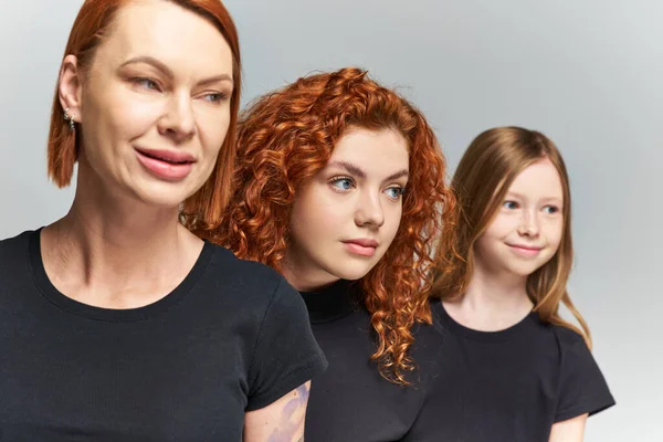 Three generations of redhead women and girl posing in matching outfits on grey backdrop, family — Stock Photo