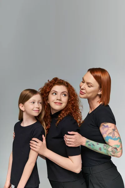 Conceito de três gerações, mulheres ruivas alegres e menina em correspondência traje abraçando em pano de fundo cinza — Fotografia de Stock