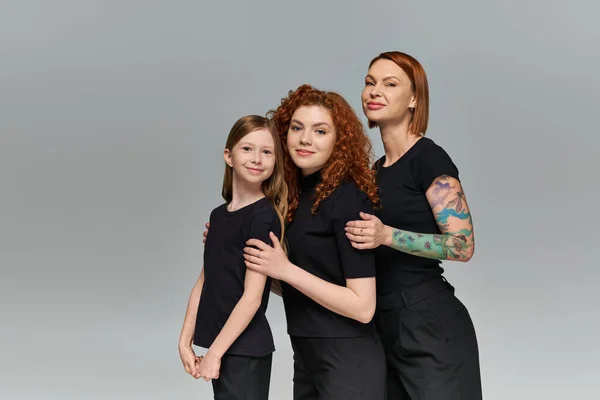 Female generations concept, happy redhead women and kid in matching attire hugging on grey backdrop — Stock Photo