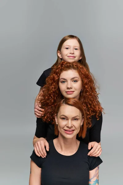 Концепція жіночих поколінь, позитивна руда сім'я в відповідному вбранні, обіймаючись на сірому фоні — стокове фото