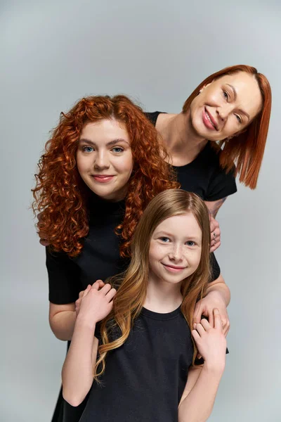 Concepto de generaciones femeninas, familia feliz con el pelo rojo posando en traje a juego sobre fondo gris - foto de stock
