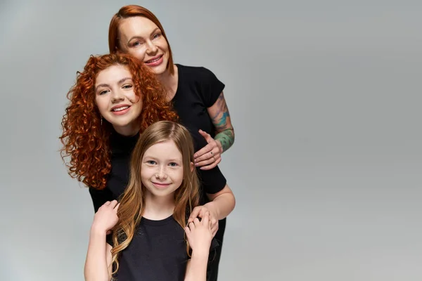 Концепція поколінь, чудова сім'я з рудим волоссям позує у відповідному вбранні на сірому фоні — стокове фото