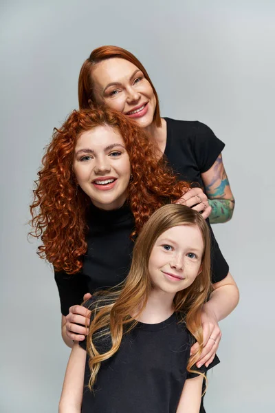 Концепція поколінь, весела сім'я з рудим волоссям позує у відповідних нарядах на сірому фоні — стокове фото