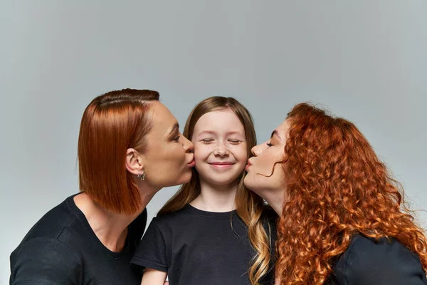 Conceito de gerações femininas, mulheres ruivas beijando bochechas sorridentes de menina no fundo cinza — Fotografia de Stock