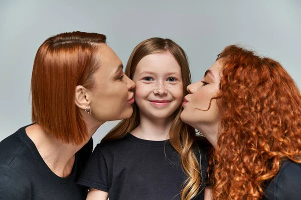 Female generations concept, redhead women kissing cheeks of freckled girl on grey background — Stock Photo
