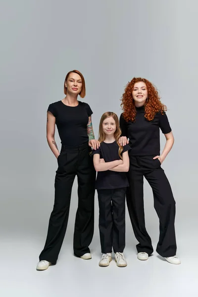 Retrato de família, três gerações de mulheres em roupas correspondentes em pé sobre fundo cinza — Fotografia de Stock