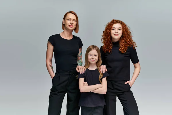 Три покоління жінок у відповідному одязі, що стоїть на сірому фоні, стильна сім'я — стокове фото